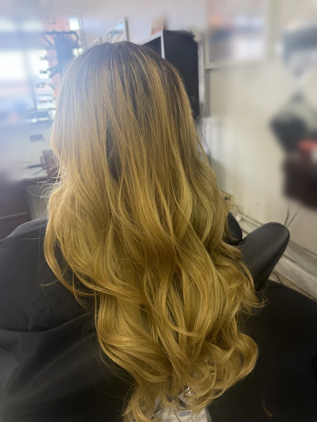Long golden blonde waves with dark roots and lighter highlights, viewed from behind.